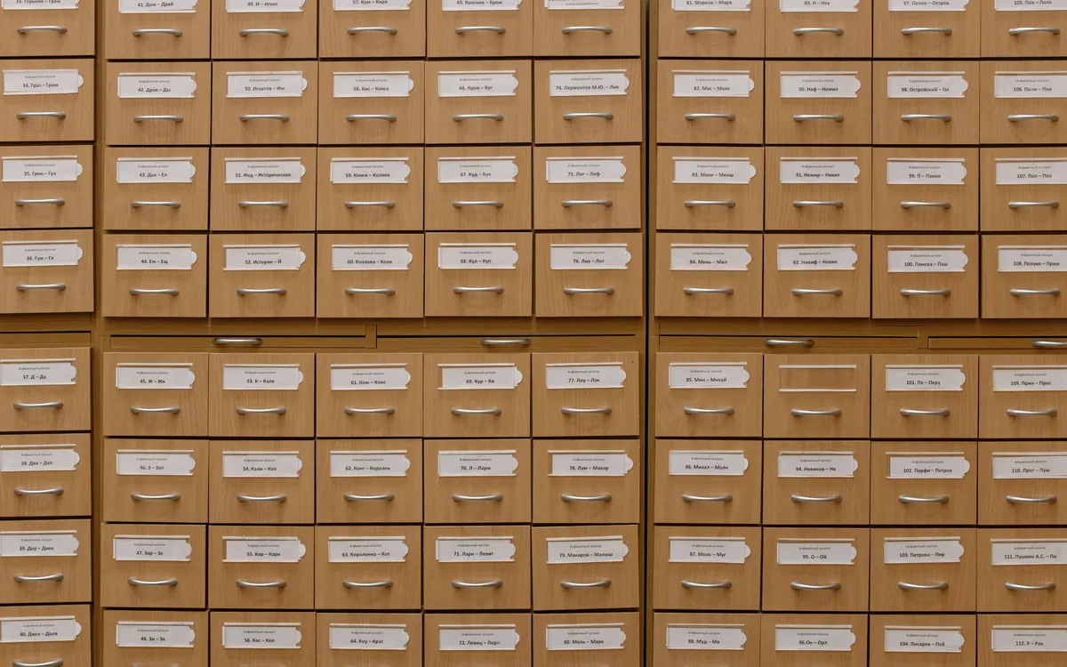 A wooden library card catalogue with rows of drawers, each with a paper label and a metal handle.