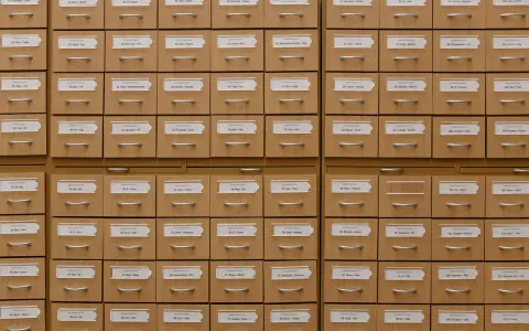 A wooden library card catalogue with rows of drawers, each with a paper label and a metal handle.
